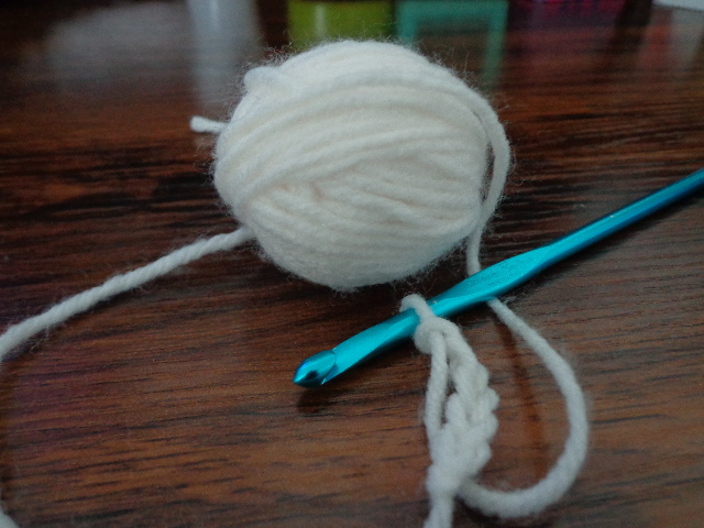 teal crochet hook with a crocheted chain of white yarn